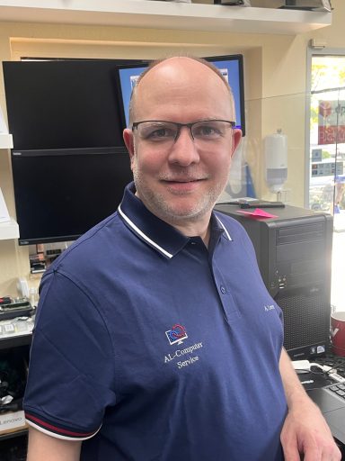 Mann mit Brille in einem Geschäft, trägt ein blaues Polohemd und lächelt.